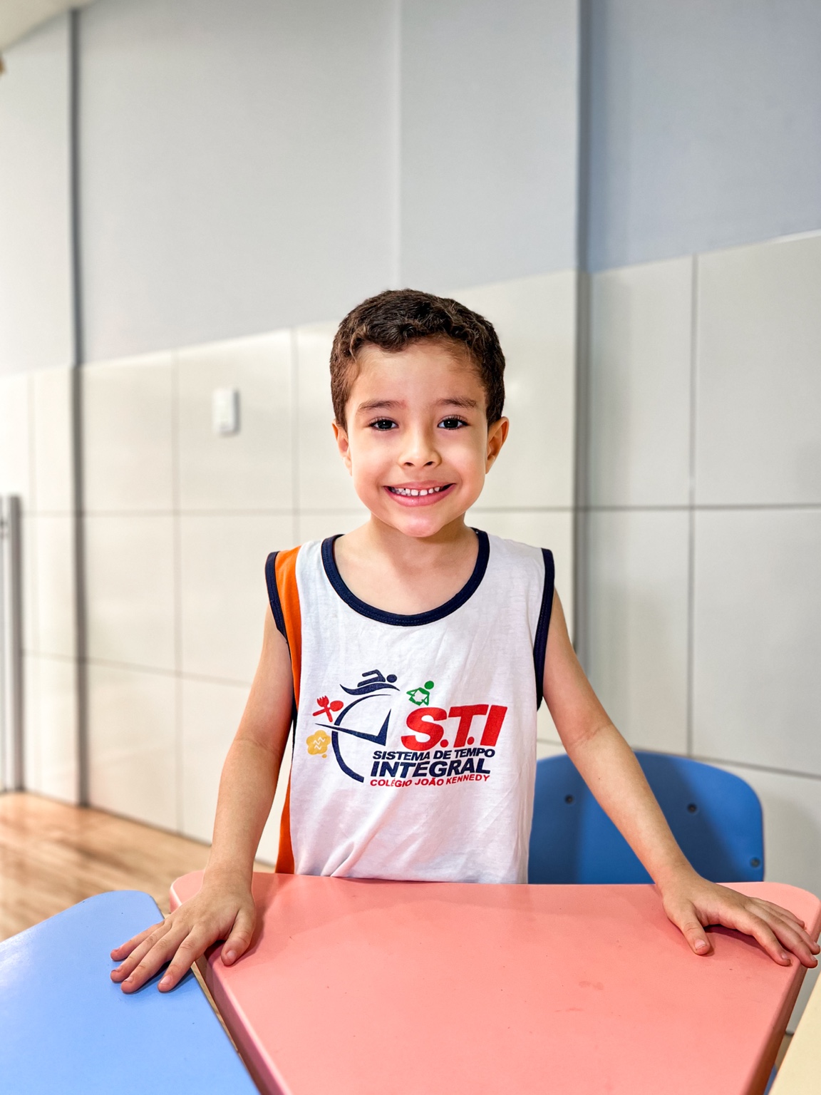 Criança com uniforme do STI sorri junto à mesa da sala