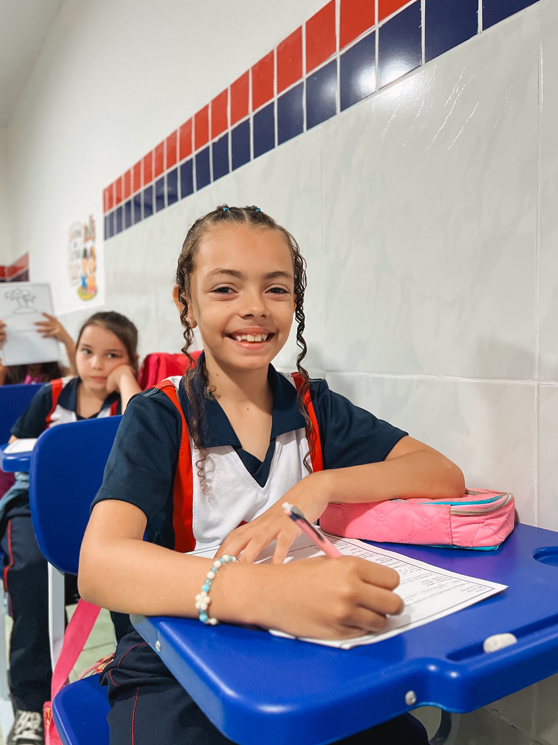 Aluna com lápis e atividade em sua carteira na sala de aula